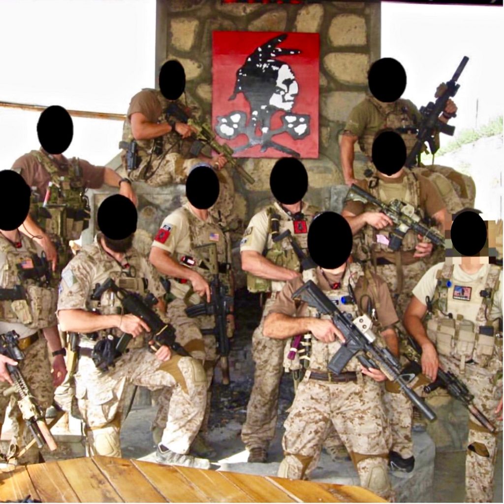 Seal Team 6 operators posing for a group picture in front of a Red Squadron emblem.